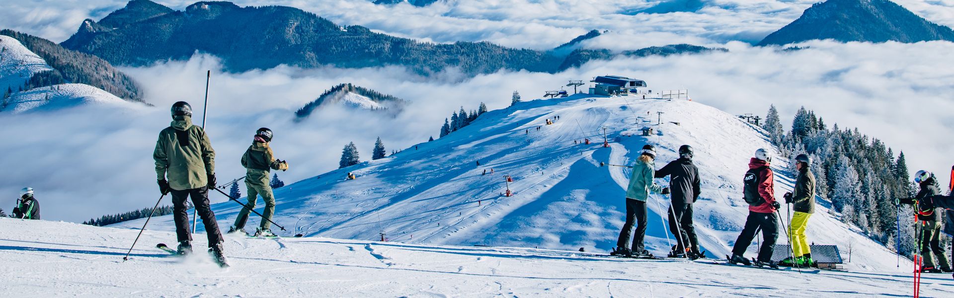 Skifahrer oben an der Piste, dahinter Nebel im Tal und Berggipfel