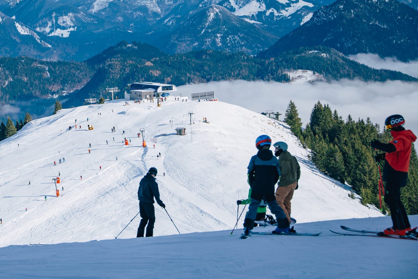 Skifahrer von hinten am Pistenrand, dahinter Berge und Nebel im Tal